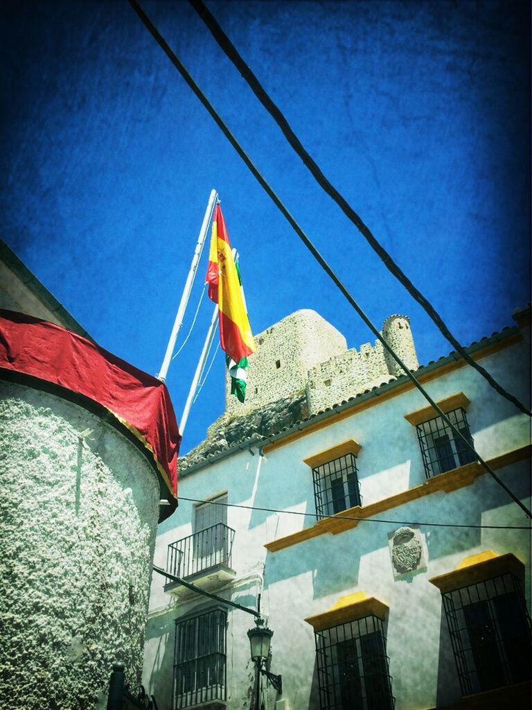 flag, building exterior, low angle view, architecture, built structure, patriotism, national flag, sky, identity, clear sky, blue, multi colored, art and craft, hanging, day, american flag, art, outdoors, animal representation, no people