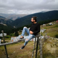 Full length of man sitting on railing against mountain