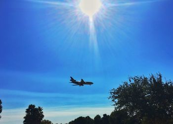 Low angle view of silhouette airplane flying against blue sky