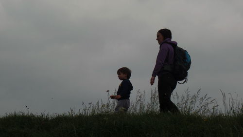 Siblings standing on field against sky