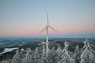 Windmill in forest against sky during sunset