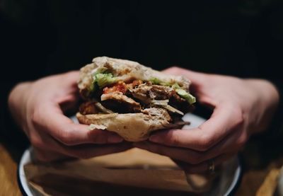 Cropped hands holding burger against black background