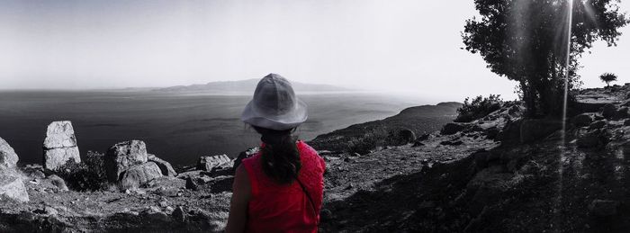 Woman on rock by sea against clear sky