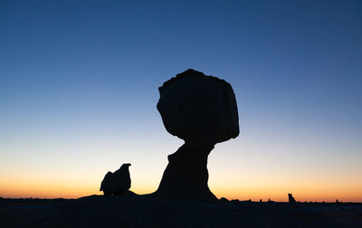 Silhouette rocks against clear sky during sunset