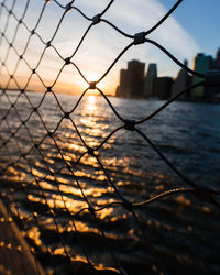 Close-up of chainlink fence against sea during sunset