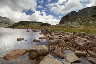 Rocks on shore by lake against sky