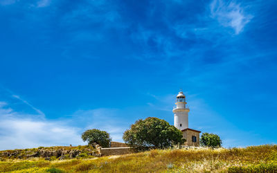 Low angle view of lighthouse on field by building against sky