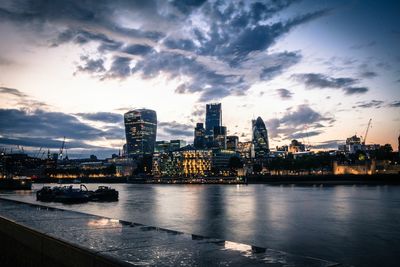 Illuminated city by river at dusk