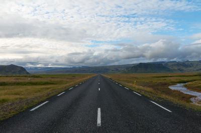 Empty road leading towards mountains against cloudy sky