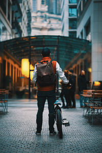 Rear view of man with bicycle standing on street amidst buildings in city