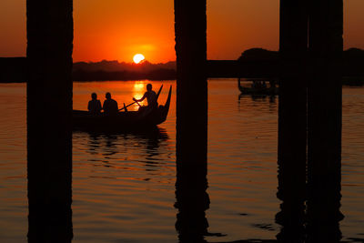 Silhouette people working on sea against sky during sunset