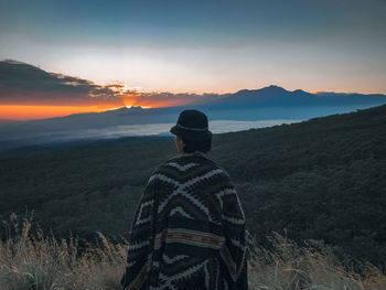 Rear view of man standing on mountain against sky