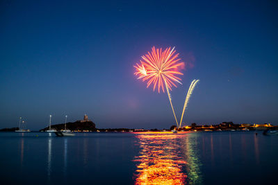 Firework display over sea against sky at night