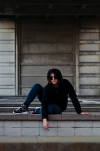 Portrait of woman wearing sunglasses while sitting below bridge