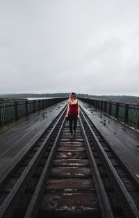 Woman walking on railroad track over rail bridge against sky