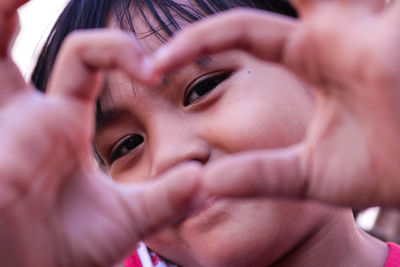 Close-up portrait of girl gesturing heart shape