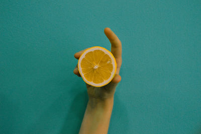 Close-up of hand holding lemon against blue background