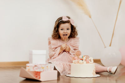 A cute little girl is sitting on the floor with a cake and gifts on her birthday.