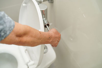 Cropped hand of man flushing toilet in bathroom
