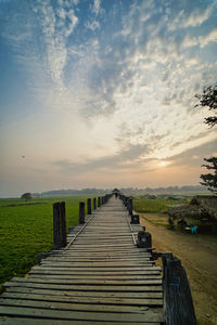 Empty boardwalk leading towards pier against sky during sunset