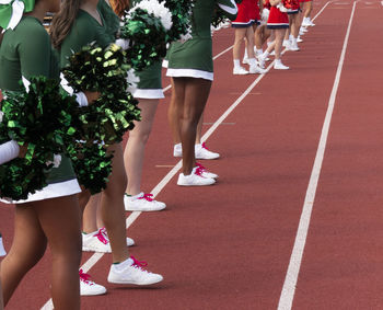 Side view of two cheerleading squads standing on sideline cheering  teams during a football game.