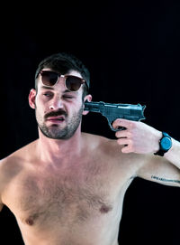 Man pointing gun in ear against black background