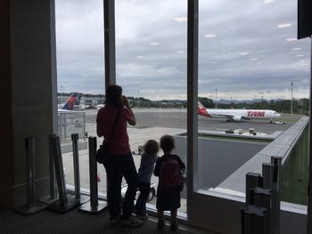 Family looking at airport runway through glass window