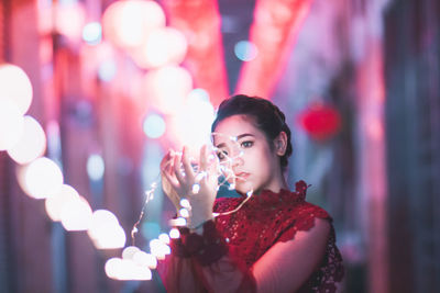 Close-up of young woman standing against illuminated lights