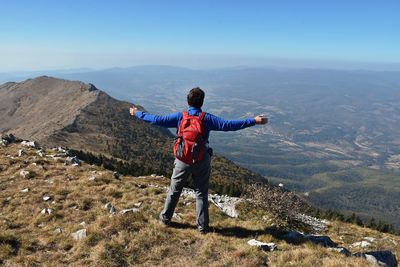 Full length of man with arms outstretched standing on mountain against sky