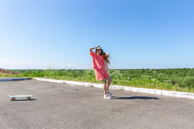 A laughing teenager girl with a skateboard in a summer trendy suit and a panama hat.