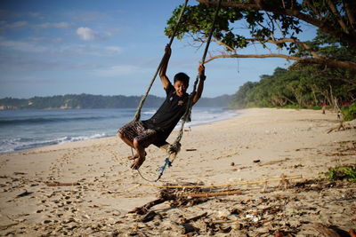 Boy on swing at beach against sky