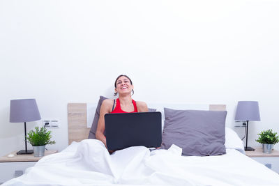 Young woman using mobile phone while sitting on bed at home