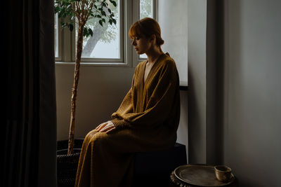 Side view of woman looking through window at home