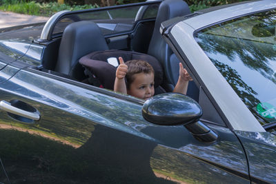 Boy gesturing thumbs up while sitting in car