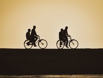 Silhouette people riding bicycle against sky during sunset