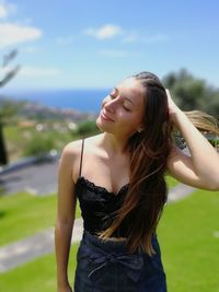 Beautiful young woman with hand in hair standing outdoors on sunny day