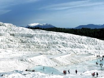 People in travertine pool against sky