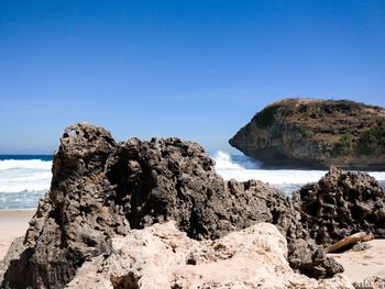 Rock formation on beach against clear blue sky