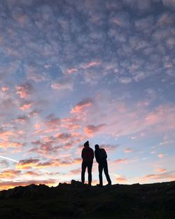 Silhouette men standing on shore against sky during sunset