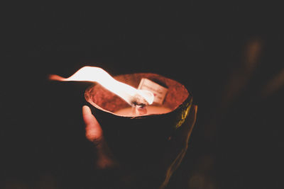 Close-up of person holding burning oil lamp in dark room