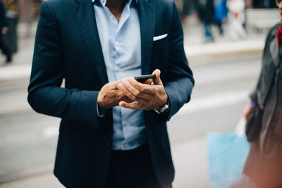 Midsection of mature businessman using smart phone while standing in city