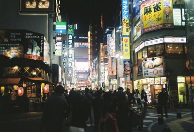 People walking on illuminated street amidst buildings in city at night