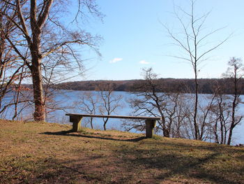 Bare trees on field by lake against sky