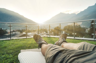 Low section of man resting on mountain against sky