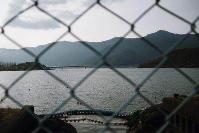 Close-up of chainlink fence by river against sky