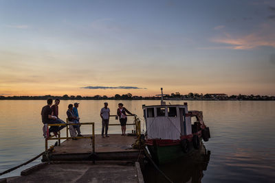 People standing on boat in sea against sky during sunset