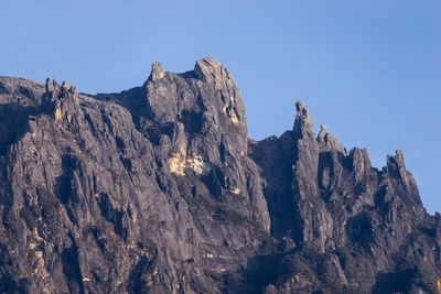 Low angle view of rocky mountains against clear blue sky