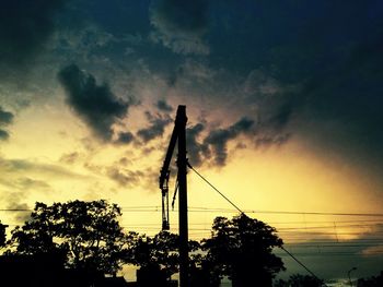 Low angle view of silhouette electricity pylon against cloudy sky