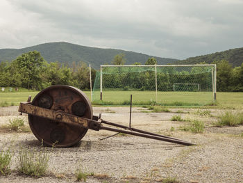 Rusty wheel on field against sky