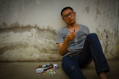 Mid adult man with drugs sitting on floor against wall